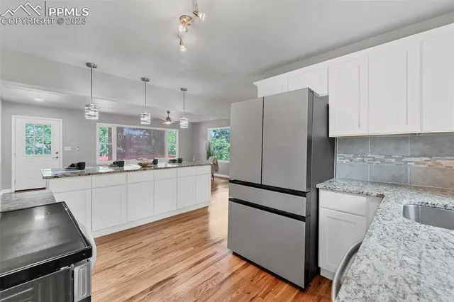 a kitchen with granite countertop a refrigerator a sink dishwasher a stove and white cabinets with wooden floor