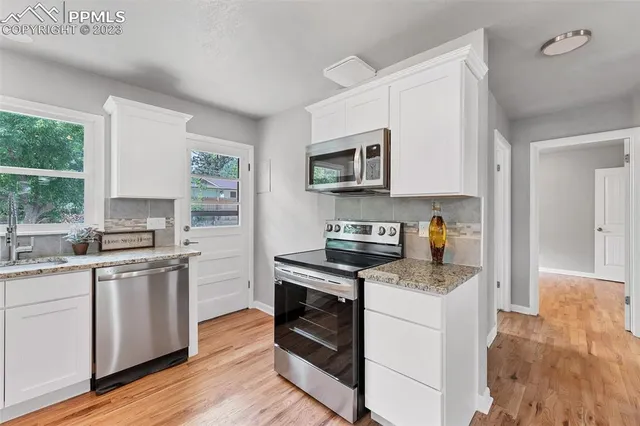 a kitchen with stainless steel appliances a stove top oven a sink a refrigerator white cabinets and wooden floor