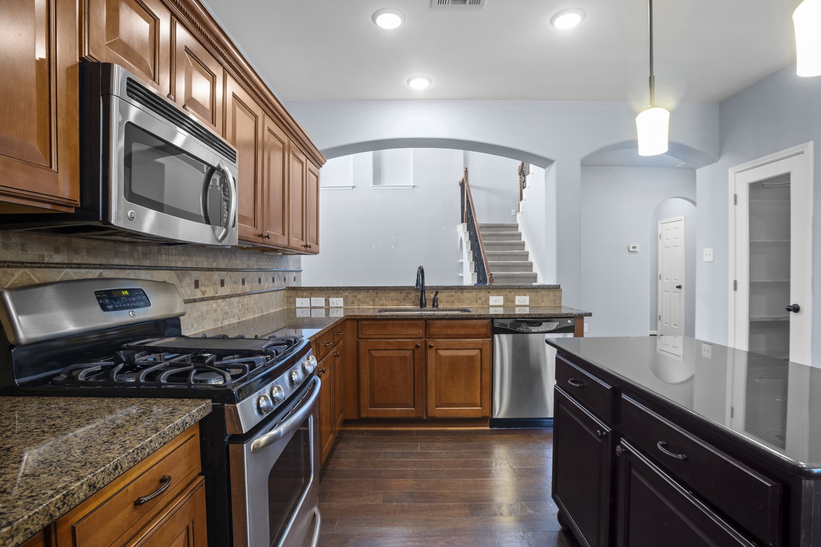 245 Razzmatazz Trail Buda, TX 78610 - Photo 11 of 40 Two tone kitchen featuring stainless steel appliances, dark wood finished floors, arched walkways, dark stone counters, and backsplash