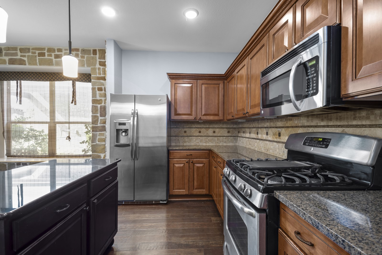 245 Razzmatazz Trail Buda, TX 78610 - Photo 12 of 40 Kitchen featuring stainless steel appliances, dark wood finished floors, hanging light fixtures, dark stone countertops, and two tone cabinets