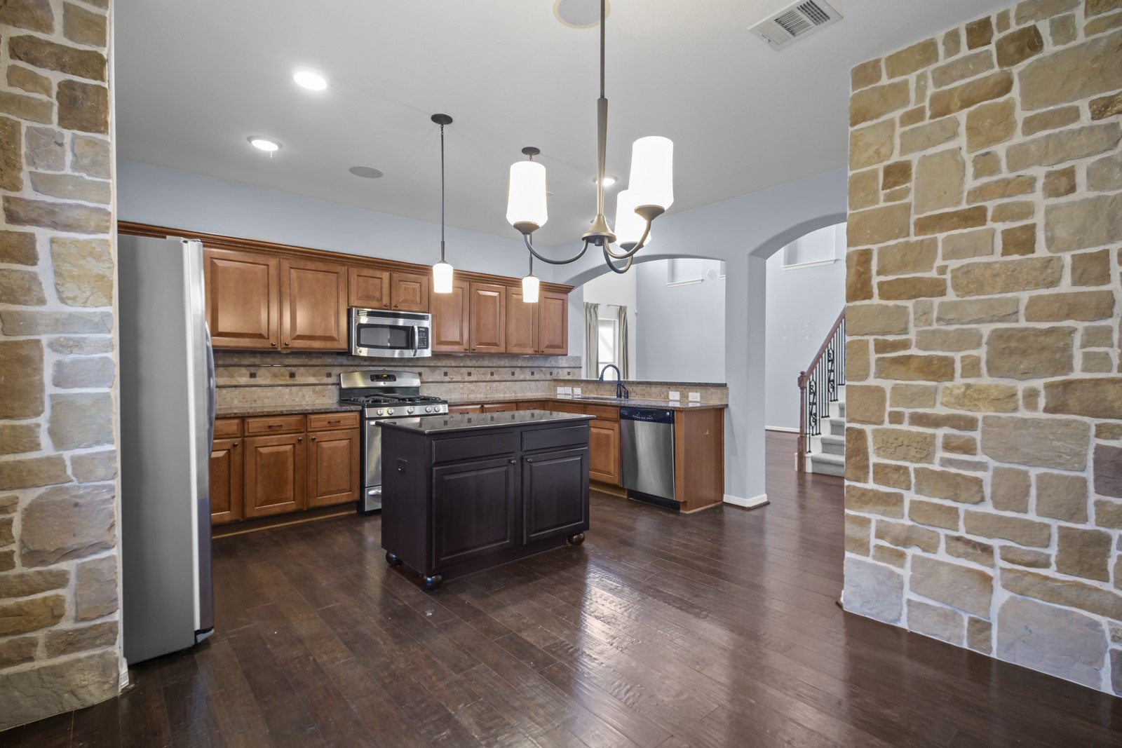 245 Razzmatazz Trail Buda, TX 78610 - Photo 14 of 40 Kitchen featuring stainless steel appliances, arched walkways, dark wood-style flooring, a peninsula, and tasteful backsplash
