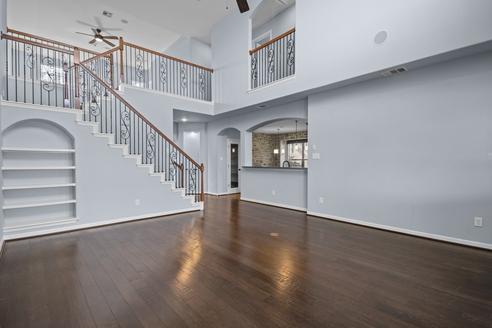 245 Razzmatazz Trail Buda, TX 78610 - Photo 17 of 40 Unfurnished living room featuring built in shelves, ceiling fan, arched walkways, dark wood-type flooring, and a high ceiling