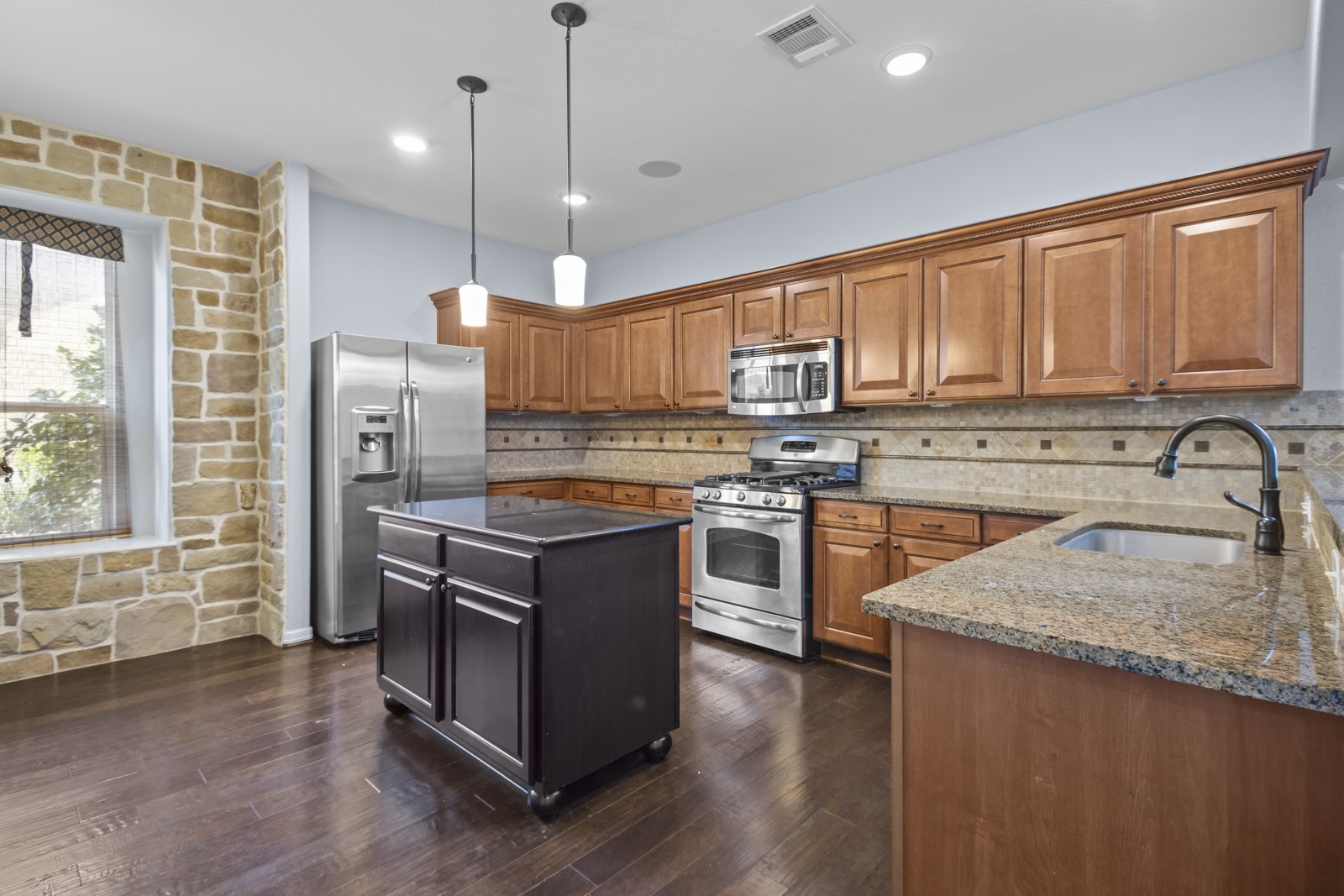 245 Razzmatazz Trail Buda, TX 78610 - Photo 8 of 40 Kitchen featuring stainless steel appliances, wood finish cabinetry, dark stone countertops, and a center island