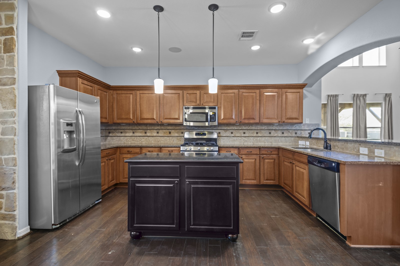 245 Razzmatazz Trail Buda, TX 78610 - Photo 9 of 40 Kitchen featuring stainless steel appliances, tasteful backsplash, a kitchen island, dark wood-style flooring, and two tone cabinets