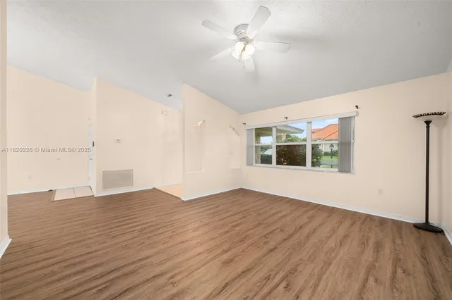 an empty room with wooden floor chandelier fan and windows