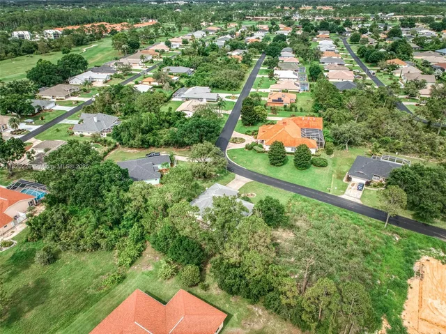 an aerial view of a house with yard and trees in the background