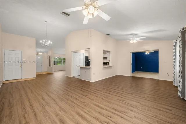 a view of an empty room with wooden floor and a kitchen