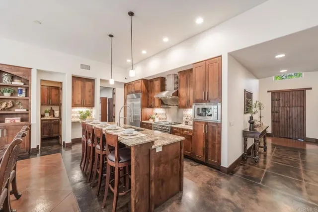a kitchen with stainless steel appliances kitchen island granite countertop a refrigerator a stove a oven a dining table and chairs with wooden floor