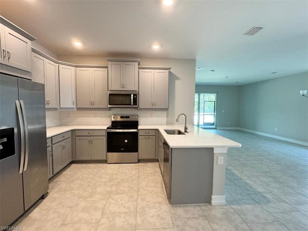 926 Enbrook Loop Naples, FL 34114 - Photo 11 of 24 Kitchen featuring gray cabinets, a peninsula, decorative backsplash, stainless steel appliances, and a sink