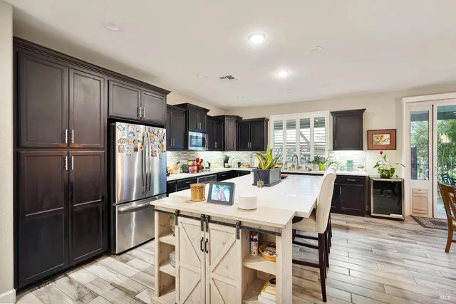 a kitchen with stainless steel appliances a dining table chairs refrigerator and cabinets