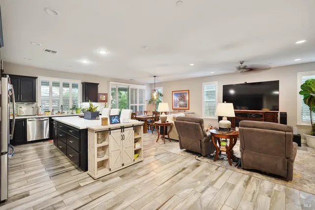 a living room with stainless steel appliances kitchen island granite countertop lots of furniture a flat screen tv and a refrigerator