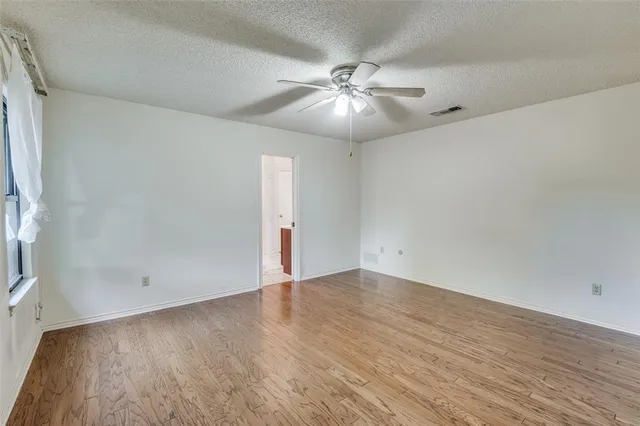 an empty room with wooden floor fan and windows