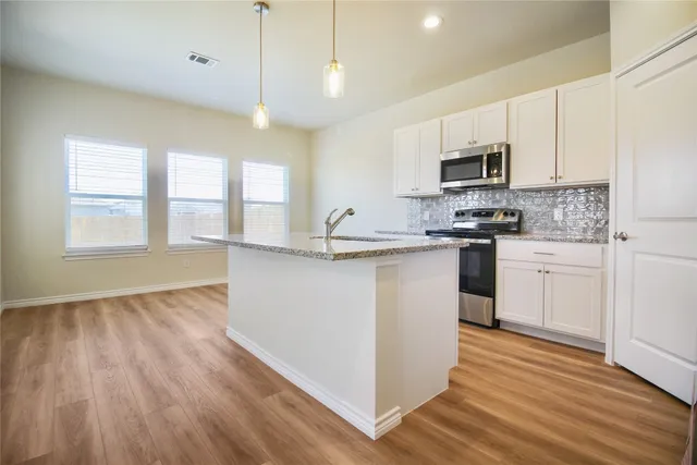 a kitchen with stainless steel appliances granite countertop a sink a stove a refrigerator and white cabinets with wooden floor