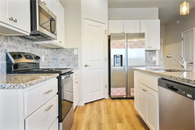 a kitchen with stainless steel appliances kitchen island granite countertop a refrigerator a sink dishwasher and a oven with white cabinets