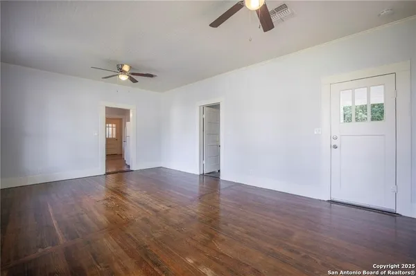 an empty room with wooden floor chandelier fan and windows