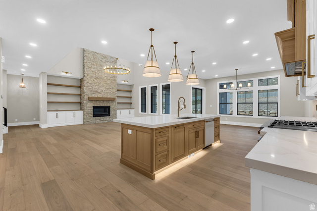 2828 Jojo Road Eagle Mountain, UT 84005 - Photo 15 of 63 Open-concept living space featuring wide-plank wood-finish flooring, a stone-faced fireplace with a wood mantle, custom built-in shelving, a large kitchen island with a sink and pendant lighting, and multiple large windows