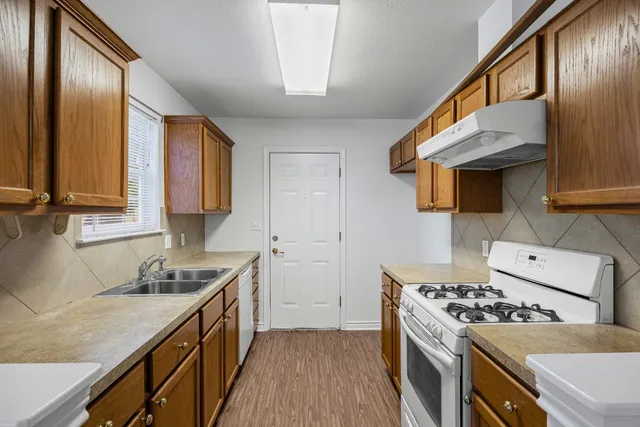 a kitchen with stainless steel appliances a stove a sink dishwasher and wooden cabinets with wooden floor