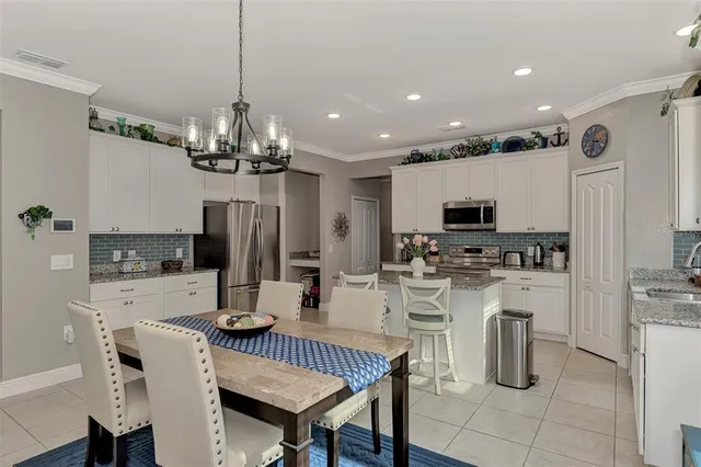 a kitchen with stainless steel appliances kitchen island granite countertop a dining table chairs refrigerator and microwave