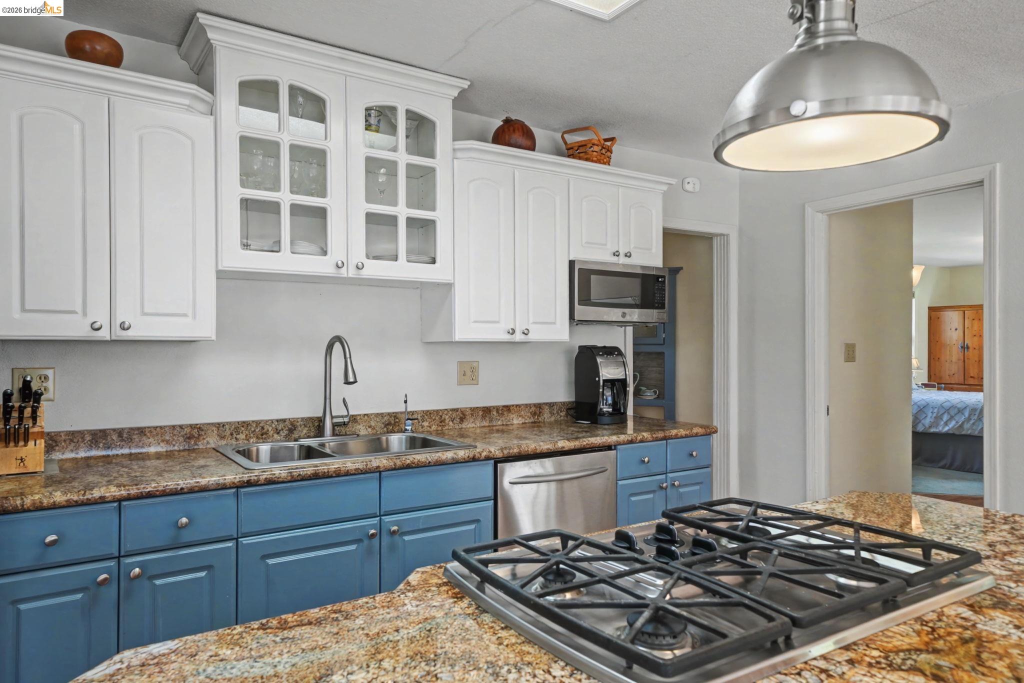 7035 Old Gulch Road San Andreas, CA 95249 - Photo 17 of 45 Kitchen with two tone cabinetry, stainless steel appliances, glass insert cabinets, dark stone countertops, and hanging light fixtures