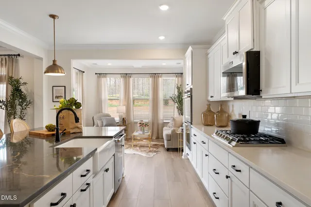 a kitchen with stainless steel appliances a sink a stove a refrigerator white cabinets and a wooden floor