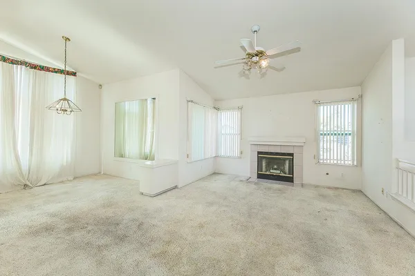 a view of an empty room with chandelier fan and fire place
