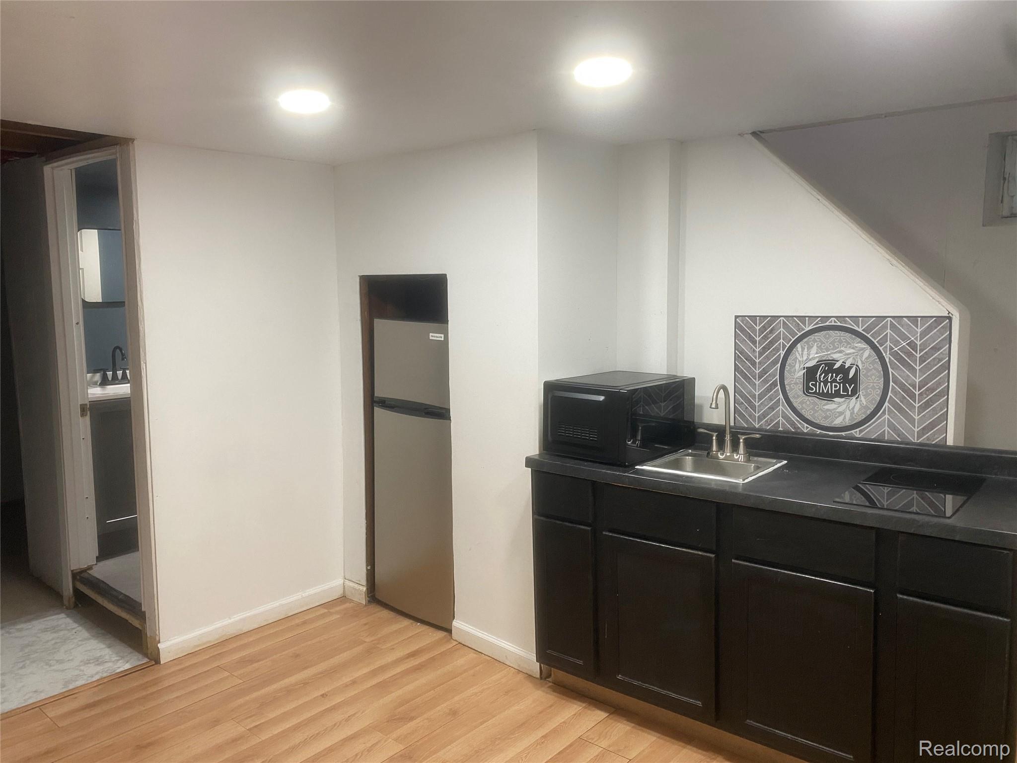 180 West Rutgers Avenue Pontiac, MI 48340 - Photo 23 of 33 Kitchen with dark cabinets, dark countertops, freestanding refrigerator, light wood-style flooring, and black microwave