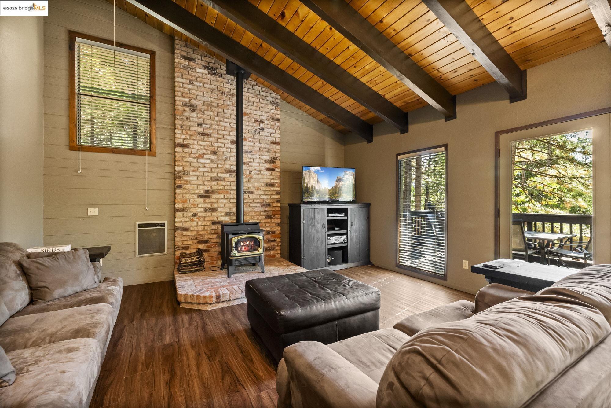 Living area with a wood stove, wood finished floors, a wooden ceiling with exposed beams, heating unit, and high vaulted ceiling