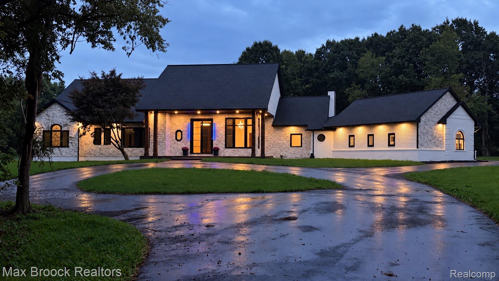 Curved driveway leading to a stone and stucco exterior with dark trim windows, covered entry, and black shingle roofing