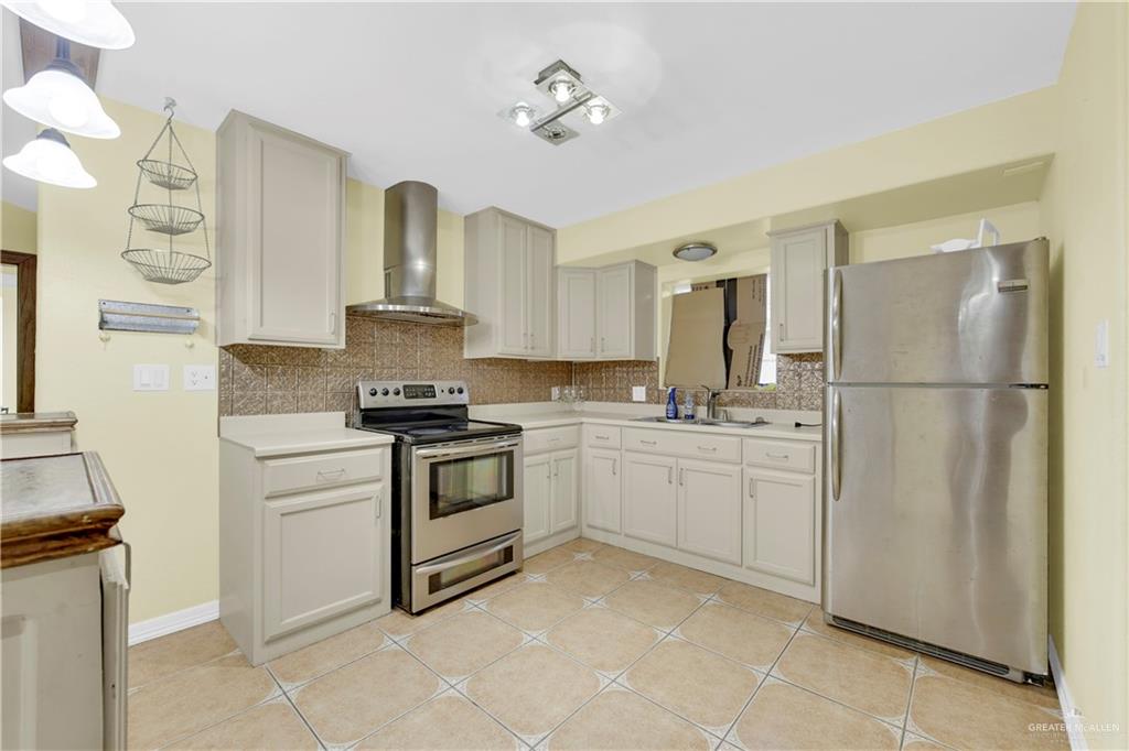 1815 Thornton Street Mission, TX 78572 - Photo 11 of 27 Kitchen with appliances with stainless steel finishes, light countertops, wall chimney exhaust hood, backsplash, and light tile patterned floors