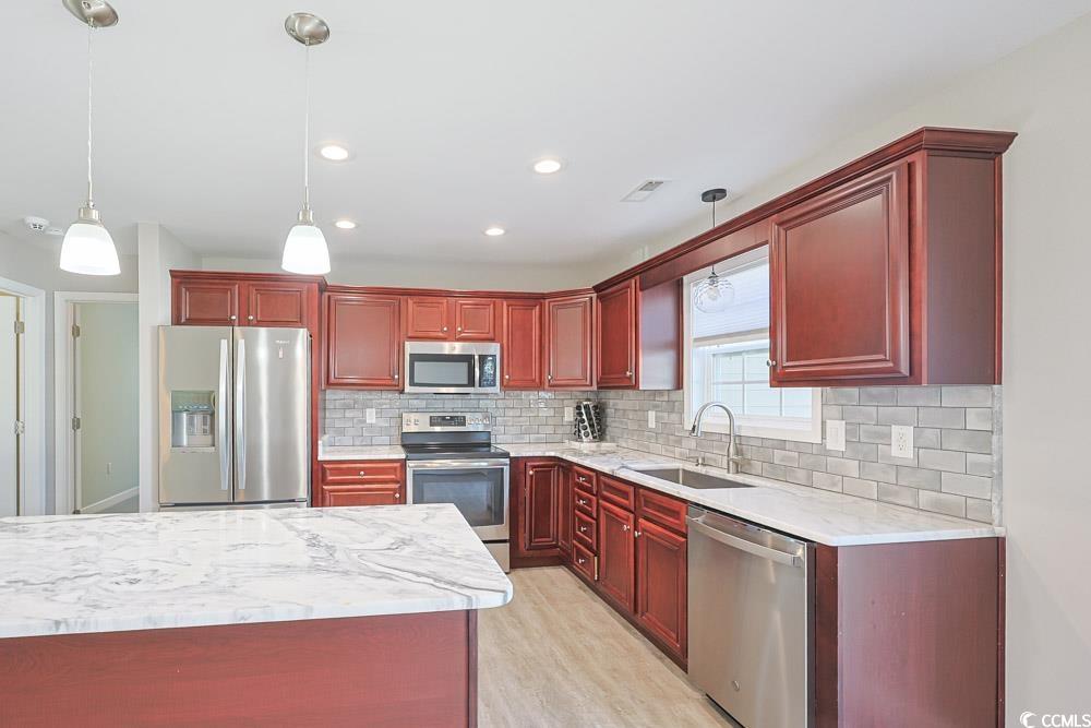 1036 Macala Drive Conway, SC 29527 - Photo 2 of 34 Kitchen with reddish brown cabinets, appliances with stainless steel finishes, light stone countertops, decorative light fixtures, and backsplash