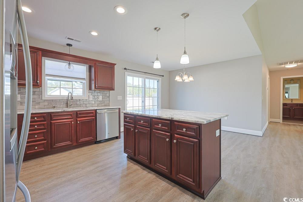 1036 Macala Drive Conway, SC 29527 - Photo 5 of 34 Kitchen featuring reddish brown cabinets, light stone countertops, decorative backsplash, stainless steel appliances, and a kitchen island