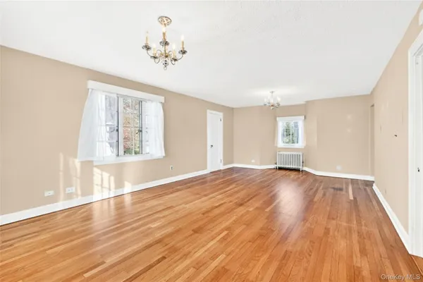 an empty room with wooden floor chandelier and windows
