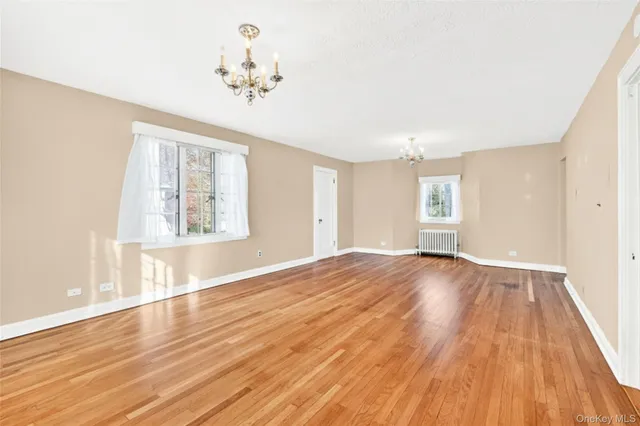 an empty room with wooden floor chandelier and windows
