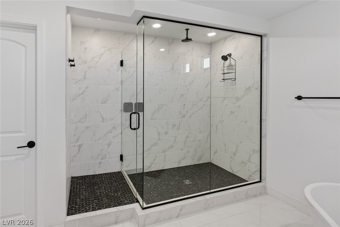 10446 Emerald Rye Street Las Vegas, NV 89183 - Photo 25 of 37 A striking glass-enclosed shower boasts a rainfall showerhead and sleek black pebble flooring.