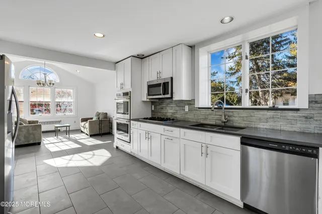 a large white kitchen with granite countertop a stove a sink a window and dining table