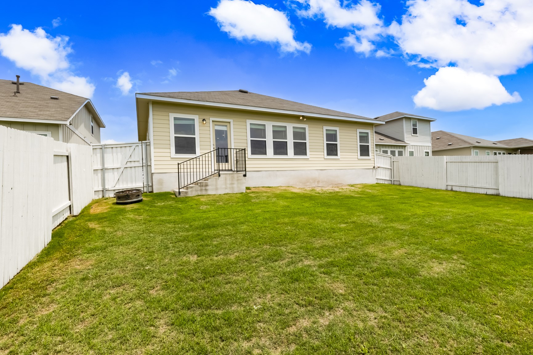2721 Winding Creek Road Kyle, TX 78640 - Photo 27 of 27 Expansive backyard featuring a lush green lawn, full perimeter fencing, a concrete patio, and a rear entry door with metal handrails
