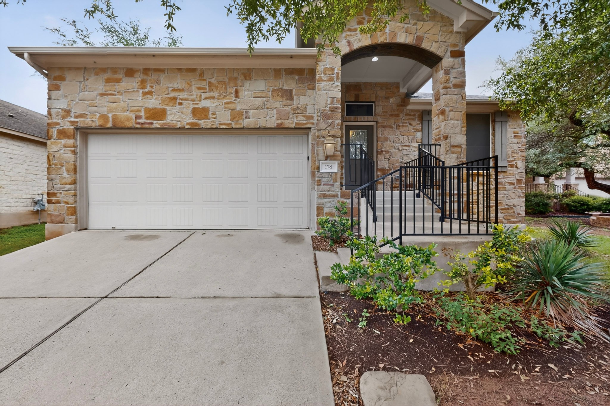 178 Limestone Trail Austin, TX 78737 - Photo 1 of 40 Stone facade exterior featuring an arched entryway, covered porch, and white paneled garage door