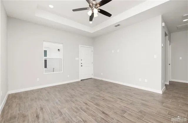 an empty room with wooden floor ceiling fan and windows