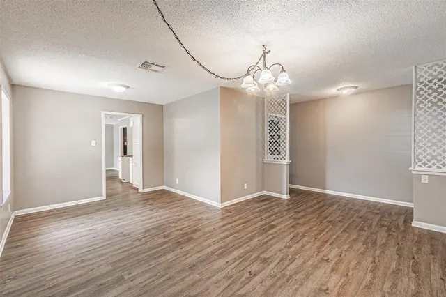 an empty room with wooden floor chandelier and windows