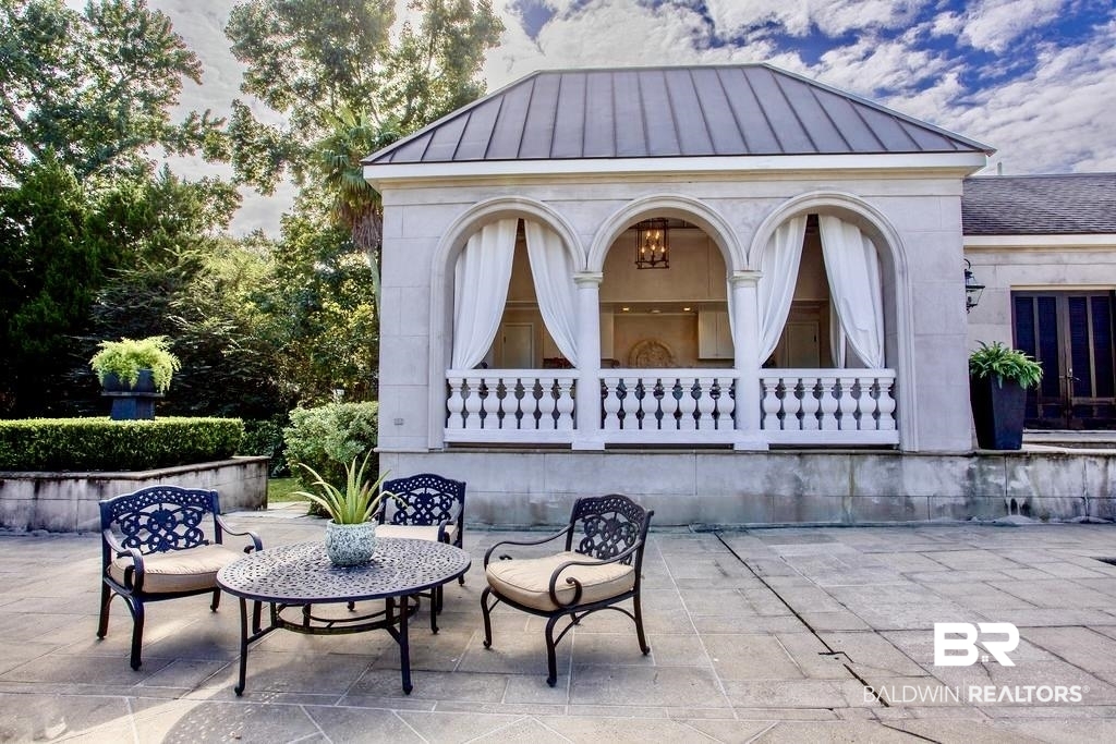 150 Austill Avenue Mobile, AL 36608 - Photo 35 of 39 Stone patio with a balustrade-adorned loggia featuring three arched openings and a metal roof