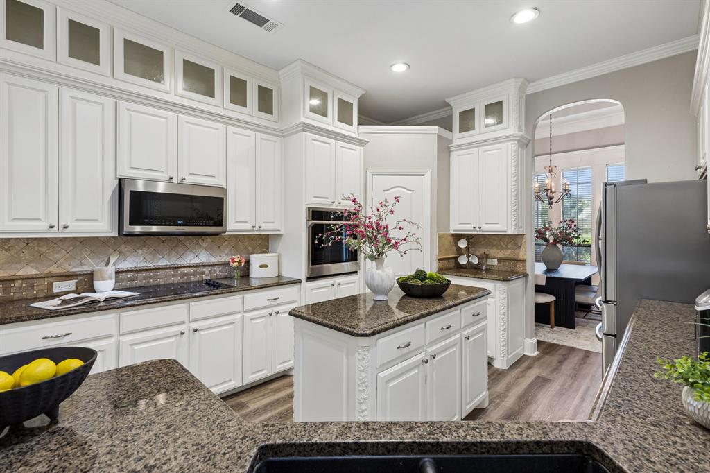 317 Singing Quail Trail Haslet, TX 76052 - Photo 10 of 32 White cabinetry with glass-front uppers, stainless steel appliances, dark speckled countertops, diamond-patterned backsplash, and wood-finish flooring