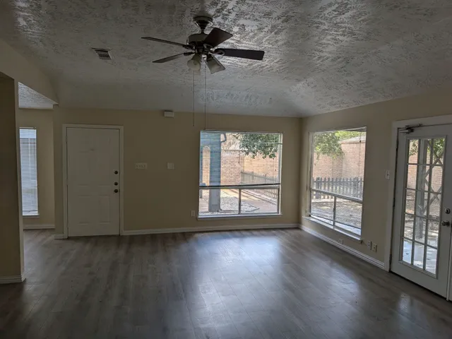 an empty room with wooden floor and windows with curtains