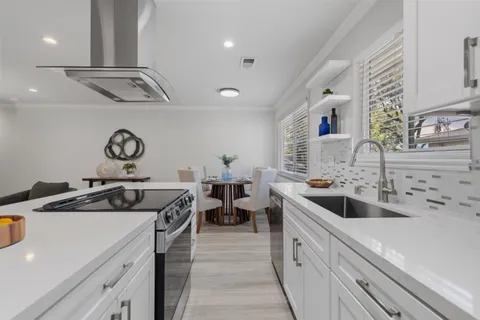 a kitchen with a sink dishwasher a stove and white cabinets with wooden floor