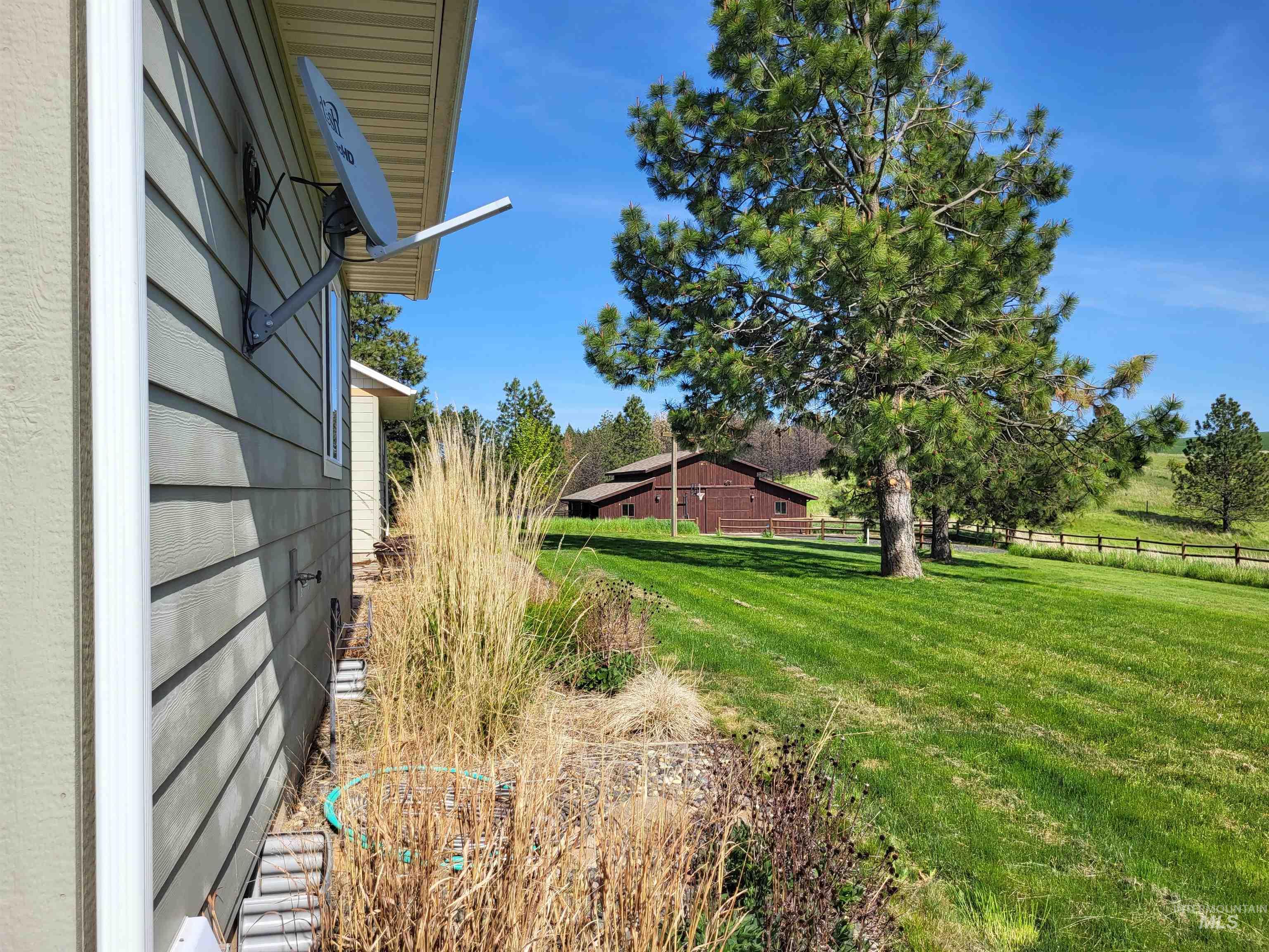 1085 Wallen Road Moscow, ID 83843 - Photo 7 of 50 Manicured lawn with mature evergreen trees, complemented by a distant barn structure and a split-rail fence