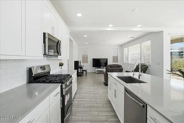 a large white kitchen with a refrigerator a stove a sink and white cabinets with wooden floor