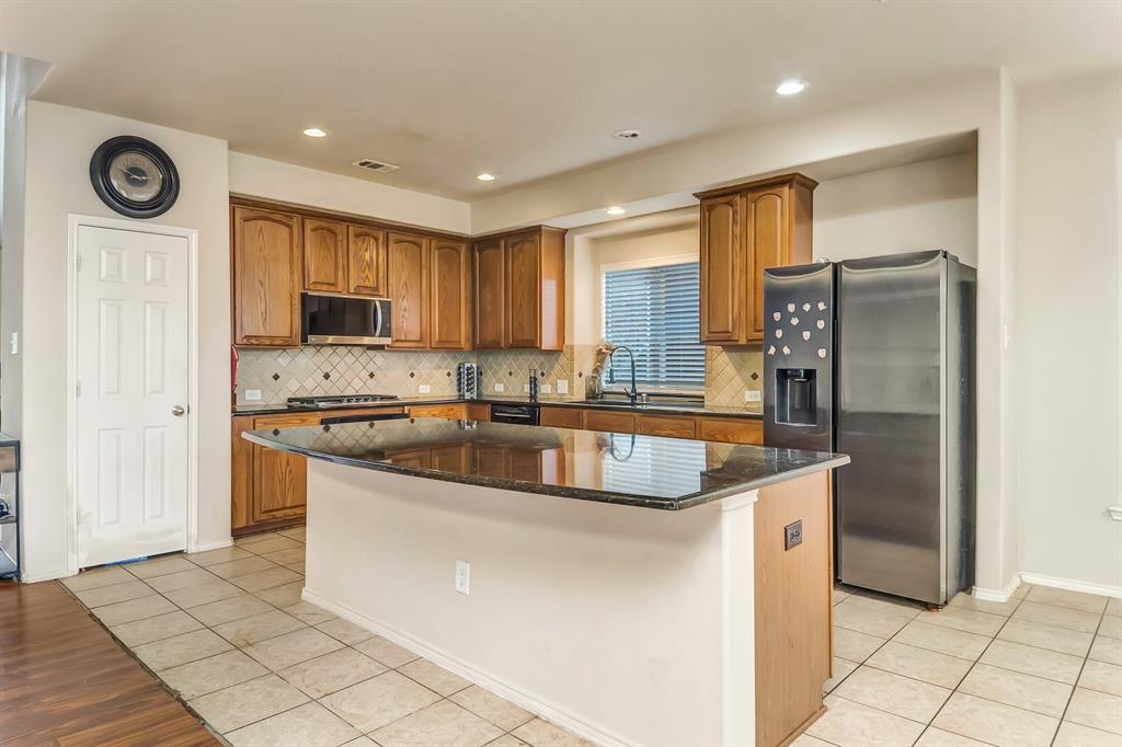 2312 Tawny Owl Road Grand Prairie, TX 75052 - Photo 15 of 40 Kitchen featuring a center island with a dark granite countertop, wood cabinetry, stainless steel appliances, and tile flooring
