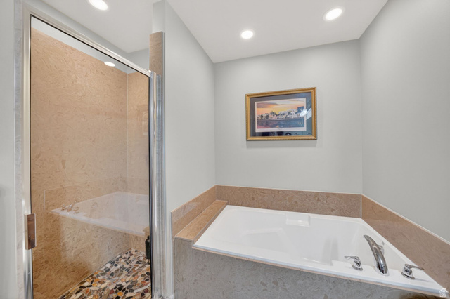 7872 Farm House Lane Midvale, UT 84047 - Photo 20 of 39 Built-in soaking tub with chrome fixtures, complemented by a glass-enclosed shower featuring natural stone-finish wall tiles and a multi-toned pebble floor