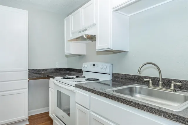 a kitchen with stainless steel appliances granite countertop a sink stove and white cabinets with wooden floor