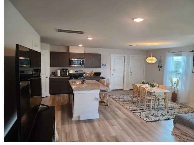 a large kitchen with stainless steel appliances kitchen island granite countertop a dining table chairs and a refrigerator