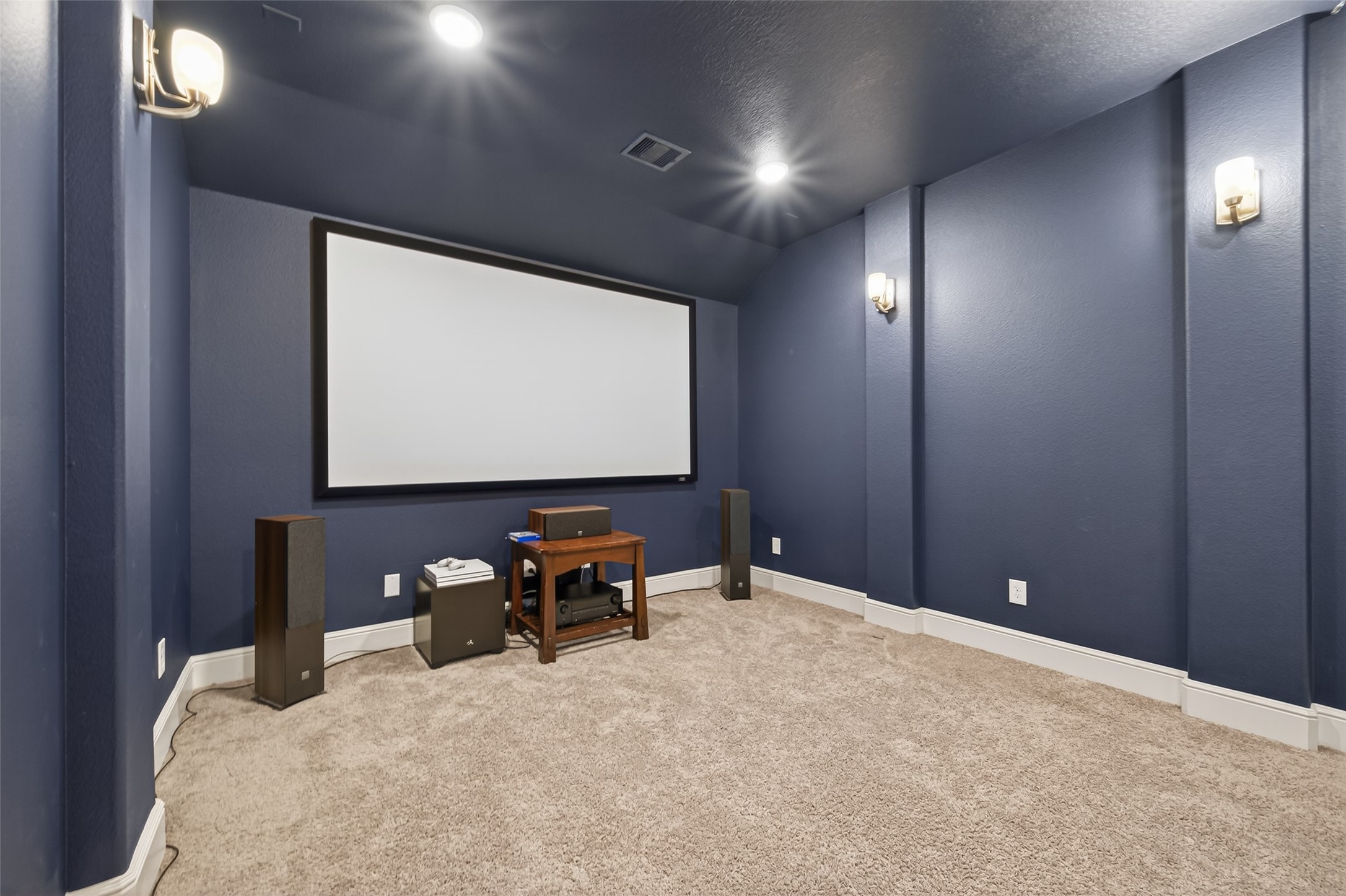 7014 Prairie Grass Lane Katy, TX 77493 - Photo 29 of 49 This photo showcases a cozy home theater room with deep blue walls, carpeted flooring, and a large screen. It's equipped with wall sconces for ambient lighting and speaker systems for an immersive viewing experience.